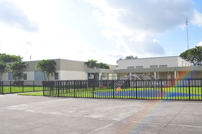 Calusa Elementary School campus with palm trees and the playground behind the front fence